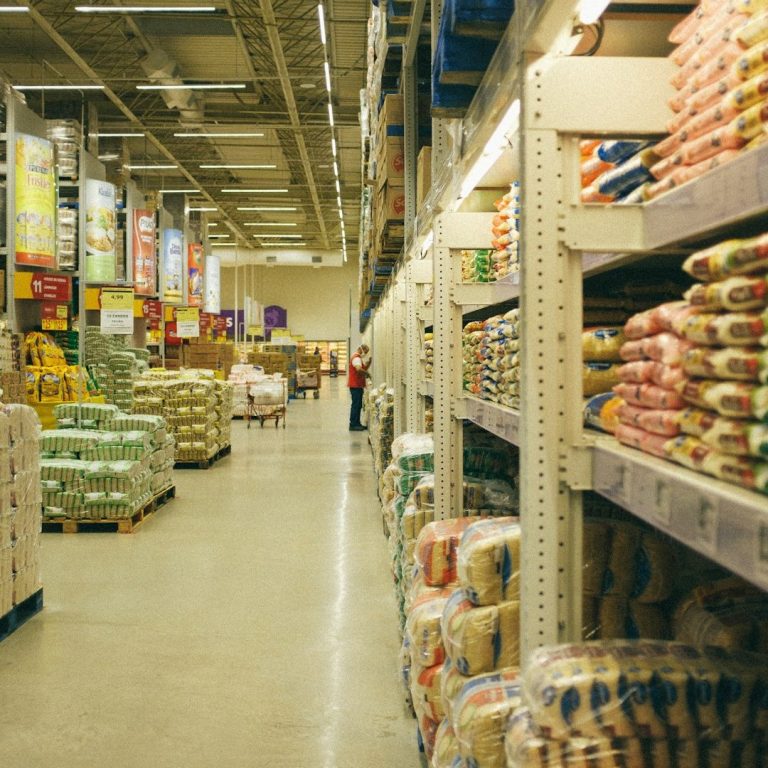 Ein breiler Gang im Supermarkt mit Regalen voller Lebensmittel und Vorräten.