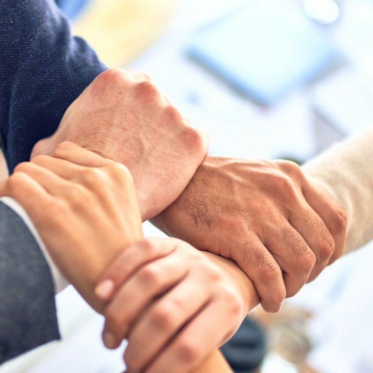 Hände verschiedener Personen, die ineinander geschlungen sind, symbolisieren Unterstützung.